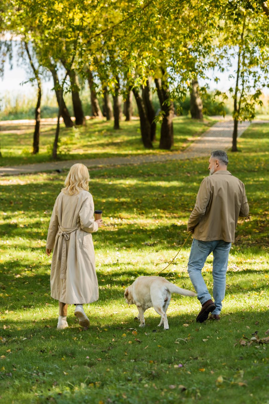 Back view of middle aged couple walking out with a dog in park during springtime.